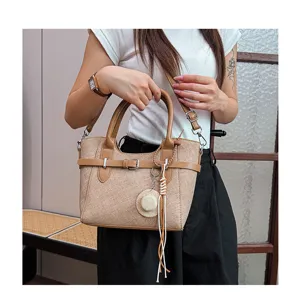 Detail shot of retro canvas tote bag with contrast leather handle and chic decorative straw hat charm.