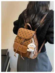 Detail view of stylish brown polka dot backpack featuring cute puppy keychain and pocket.