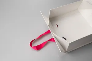 Detail shot of white foldable gift box corner with hot pink ribbon handle close up.