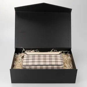 Detailansicht der schwarzen Faltgeschenkbox mit Strohfüllung und karierter Clutch-Tasche.
