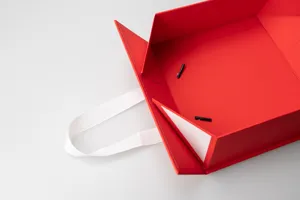 Red folding gift box detail view, large cardboard packaging with white ribbon handle.