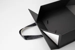 Black foldable gift box detail shot, premium rigid paper packaging box with ribbon handle.