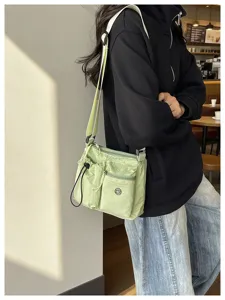 Detailed shot of a light green nylon crossbody bag with multiple pockets in a casual setting.