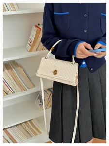 Detail shot of white woven crossbody bag with metal lock, lifestyle shelf background.