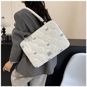 Detailed shot of white quilted laptop bag with blue bow embroidery, stylish shoulder carry.