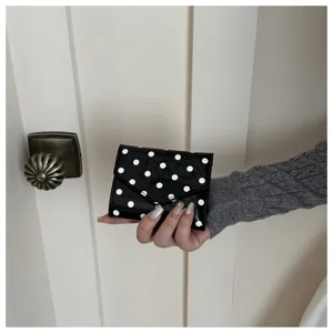 Primo piano di un piccolo portafoglio nero a pois bianchi tenuto in mano, bel dettaglio.