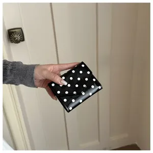 Vista dettagliata del motivo a pois bianco e nero sul portafoglio compatto da donna.