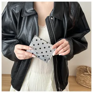 Primo piano del portafoglio argento a pois tenuto in mano, evidenziando il design compatto.
