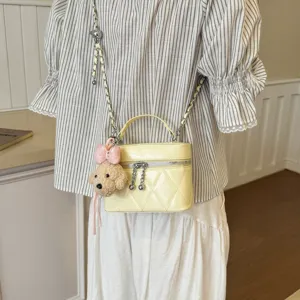 Detail shot of women yellow quilted box bag with chain strap and cute plush charm pendant.
