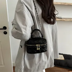 Black quilted vanity bag detail showcasing classic chain strap, top handle and golden zippers.