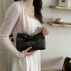 Detailed view of the elegant black leather bow clutch bag held by model in indoor setting.