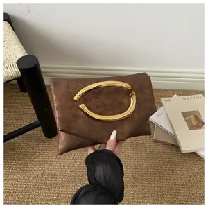 Close-up of brown clutch bag featuring a striking oversized golden loop handle and unique texture detail.