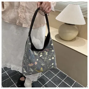 Primer plano del bolso gris bordado con flores mostrando delicados detalles de mariposas.