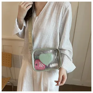 Vue détaillée du sac bandoulière en PVC transparent avec écusson cœur vert et large sangle.