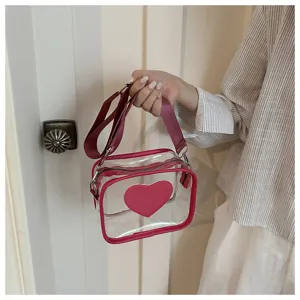 Détail de sac bandoulière en PVC transparent avec appliqué cœur rose et bandoulière large.