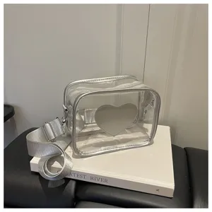 Sac bandoulière transparent en PVC avec sangle large argentée et détail cœur élégant.