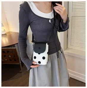 Detail view of a chic black and white polka dot crossbody phone bag worn by a model.