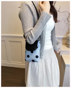 Detail shot of the contrast color polka dot crossbody phone bag worn by a model in summer outfit.