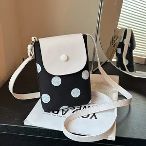 Black and white polka dot crossbody phone bag with white flap and adjustable strap for women.