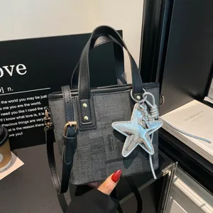 Stylish denim bucket shoulder bag with silver star pendant and black leather handles detail.