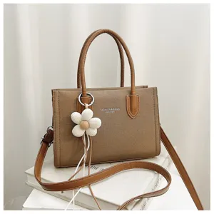 Detailansicht der braunen Canvas-Tasche mit stilvollem Blumenanhänger und Ledergriffen.