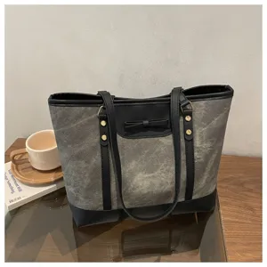 Detail shot of dark grey canvas tote bag with black leather trim and cute bow on wooden desk.