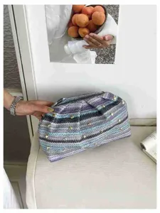 Λεπτομέρεια από κομψή υφαντή τσάντα φάκελο με μεταλλικά τρουκς, ιδανική για διακοπές.