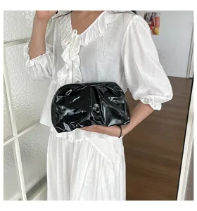 Détail élégant d'un sac clutch noir en cuir vernis brillant chic tenu par un modèle.