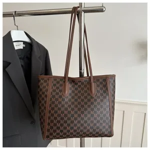 Detail view of large capacity monogram tote bag with brown leather trim and shoulder straps.