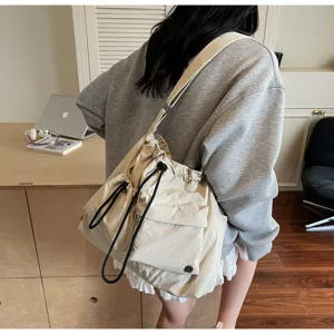 Detail shot of beige nylon drawstring shoulder bag showing wide strap and front pocket structure.