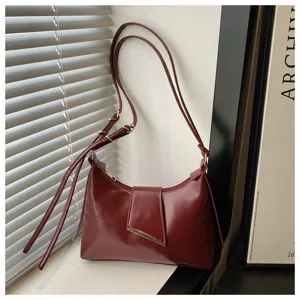 Detailed view of this chic burgundy underarm bag featuring glossy leather and metal hardware.