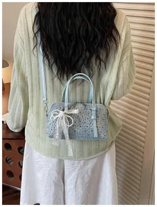 Details of the stylish light blue denim handbag featuring metal studs and white lace bow.