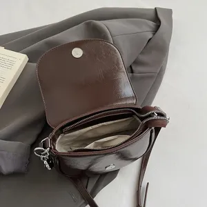 Chic brown patent leather crossbody bag detail, compact mini saddle bag with metal clasp and zip.
