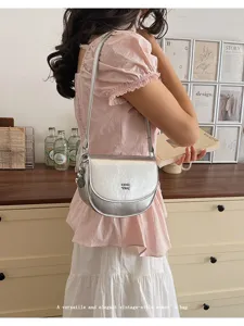 Silver metallic saddle shoulder bag with delicate strap and modern minimalist design details.