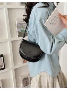 Detail view of a stylish black vintage saddle shoulder bag worn by a model in casual wear.