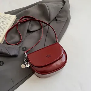Detailed view of the dark red patent leather crossbody bag with chic metallic charm and strap.