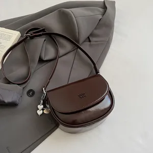 Chic dark brown patent leather saddle shoulder bag with heart charm and slim strap.