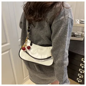 Detail view of a stylish white shoulder bag with black trim and cute red cherry charm.