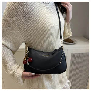Detailed view of women black shoulder bag featuring cute cherry charm and golden chain strap.
