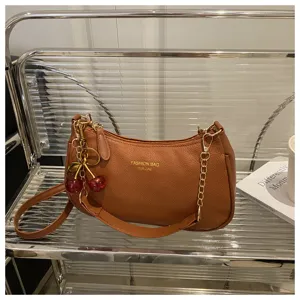 Brown leather shoulder bag detail, stylish cherry charm and gold chain accessory close up.