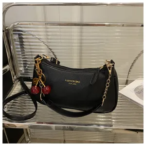 Detailed view of the stylish black shoulder bag featuring gold chain and cute cherry charm.