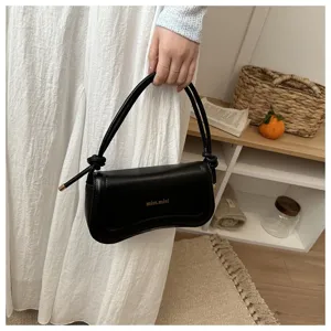 Minimalist black underarm shoulder bag detail showing sleek leather texture and knotted strap.