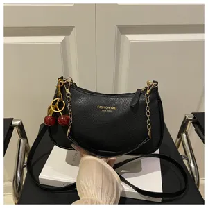 Detailed view of black leather shoulder bag with gold chain and cute cherry charm accessory.