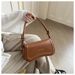 Detail view of stylish brown leather underarm shoulder bag with trendy knotted handle design.