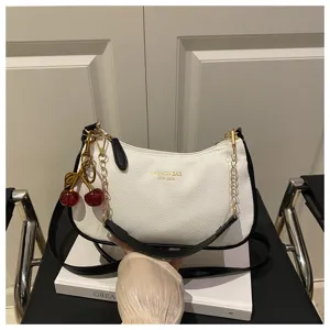 Trendy white shoulder crossbody bag with black trim and cute cherry pendant detail view.