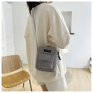 Grey corduroy crossbody bag detail view, casual lifestyle wearing shot showing pocket design.