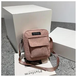 Detail shot of the pink corduroy crossbody bag showing front pocket and woven label texture.