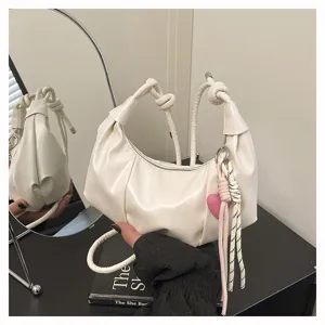White leather underarm shoulder bag featuring unique knot strap and sweet heart pendant.