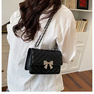Close-up detail of stylish women's black quilted chain shoulder bag with elegant bow accent.