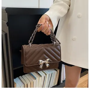 Brown quilted shoulder bag with metal chain strap and elegant bow decoration, detailed view.